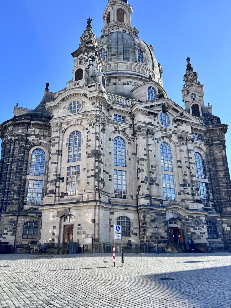 A low-angle view of a historic church with a large dome and ornate architecture, featuring intricate stonework and large windows, set against a clear blue sky.