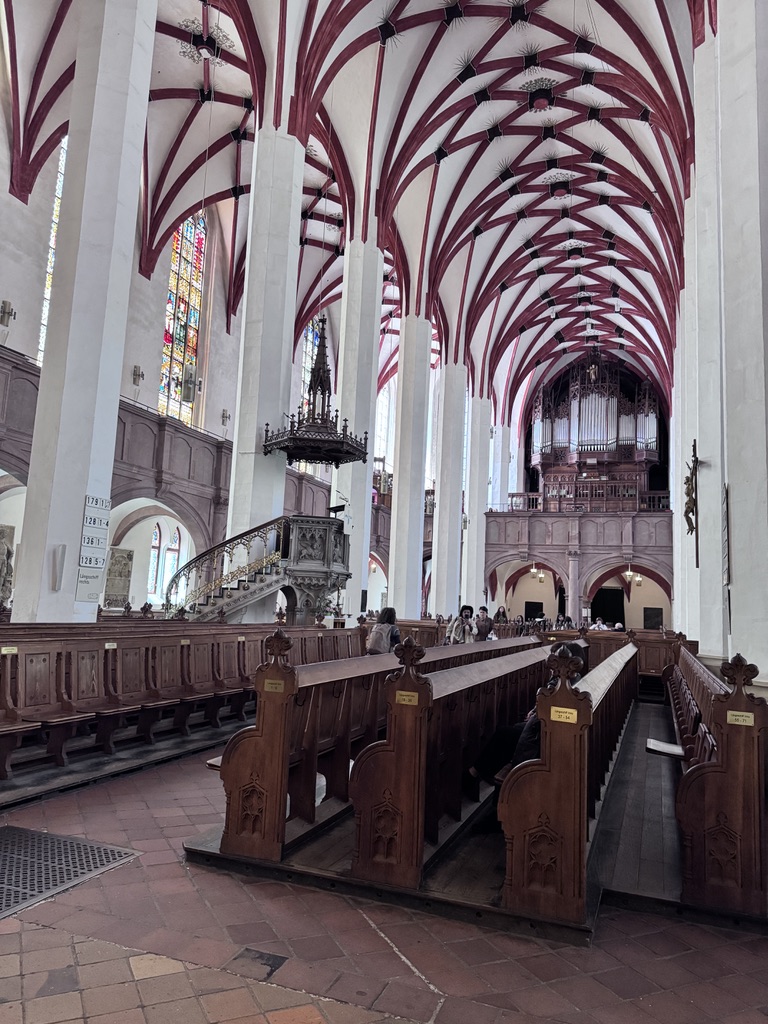 Interior view of a church showcasing high ceilings with red and white arches, wooden pews, and stained glass windows.