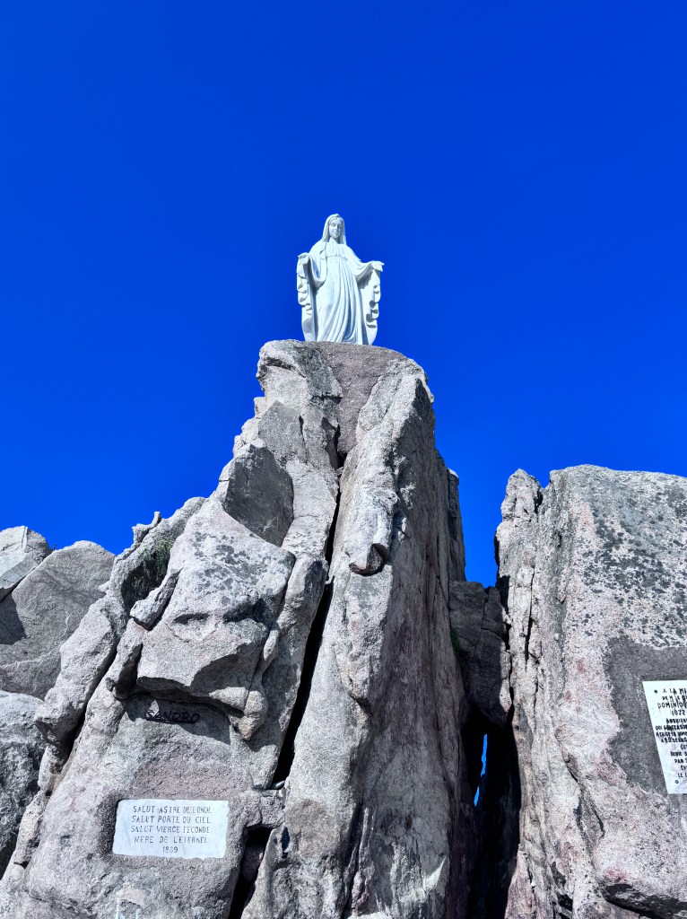 Statue of a figure standing on a rocky outcrop against a clear blue sky.