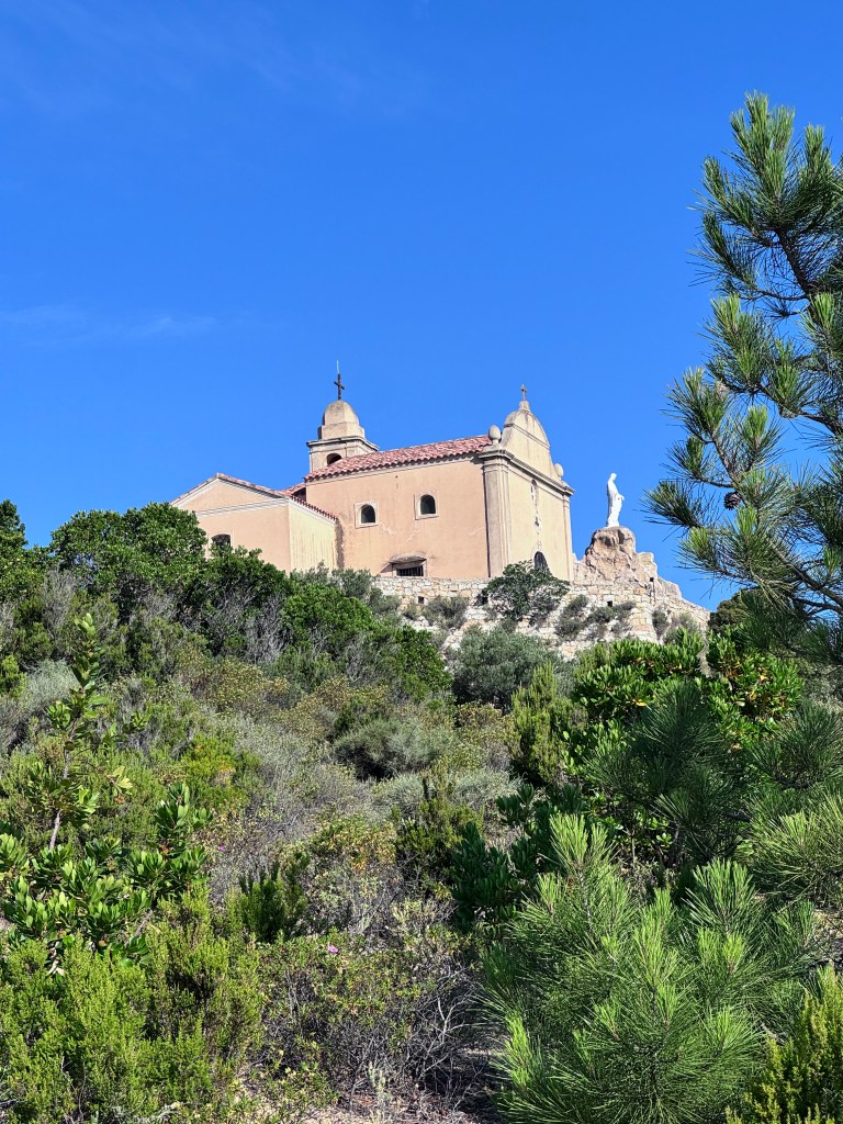 A historic church perched on a hillside, surrounded by greenery and a clear blue sky.