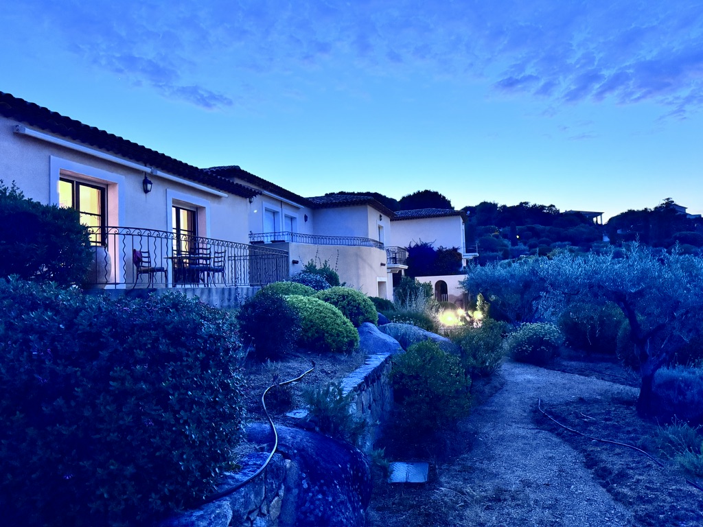 A beautiful exterior view of a house during twilight, surrounded by lush greenery and elegantly lit windows, creating a serene atmosphere.