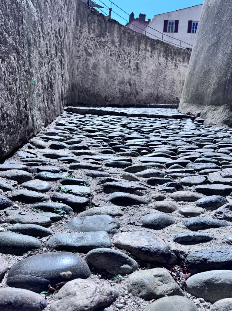 Close-up view of a cobblestone pathway between two stone walls, with sunlight illuminating the textured stones.