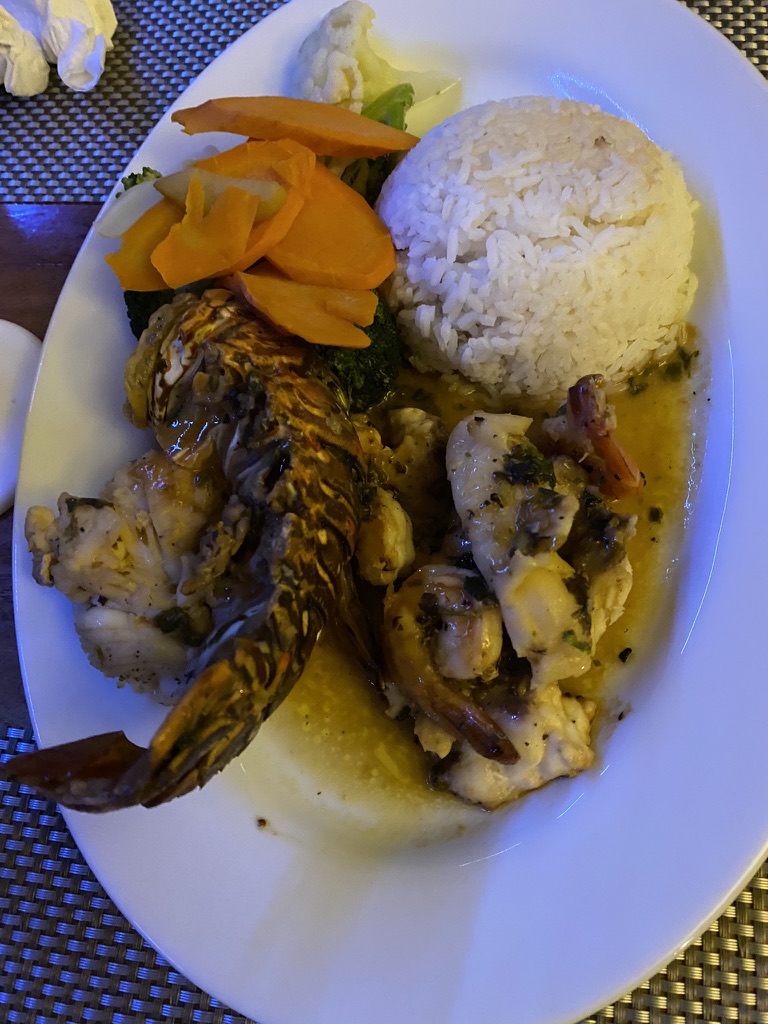 A plated dish featuring lobster, shrimp, and white rice accompanied by steamed vegetables such as broccoli, cauliflower, and carrots, served in a flavorful sauce.