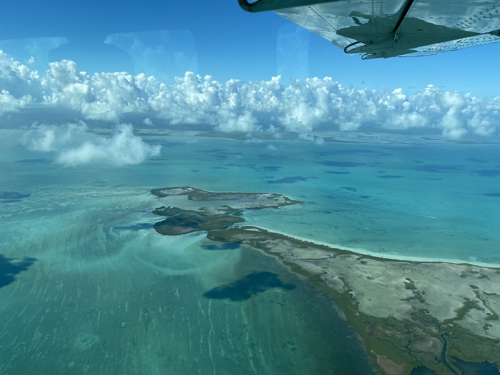 Aerial view of turquoise waters and small islands under a clear blue sky with scattered clouds.
